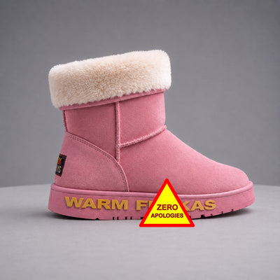A pink suede ankle boot with a fluffy cream shearling-style trim at the top, shown on a grey studio background. The outsole has gold lettering branding along the sole and a red-and-yellow warning-style triangle sticker with the words 'ZERO APOLOGIES' is placed in front of the boot.