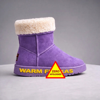 A purple suede ankle boot with a wool cream cuff trim at the top, shown on a grey studio background. The outsole has gold lettering branding along the sole and a red-and-yellow warning-style triangle sticker with the words 'ZERO APOLOGIES' is placed in front of the boot.