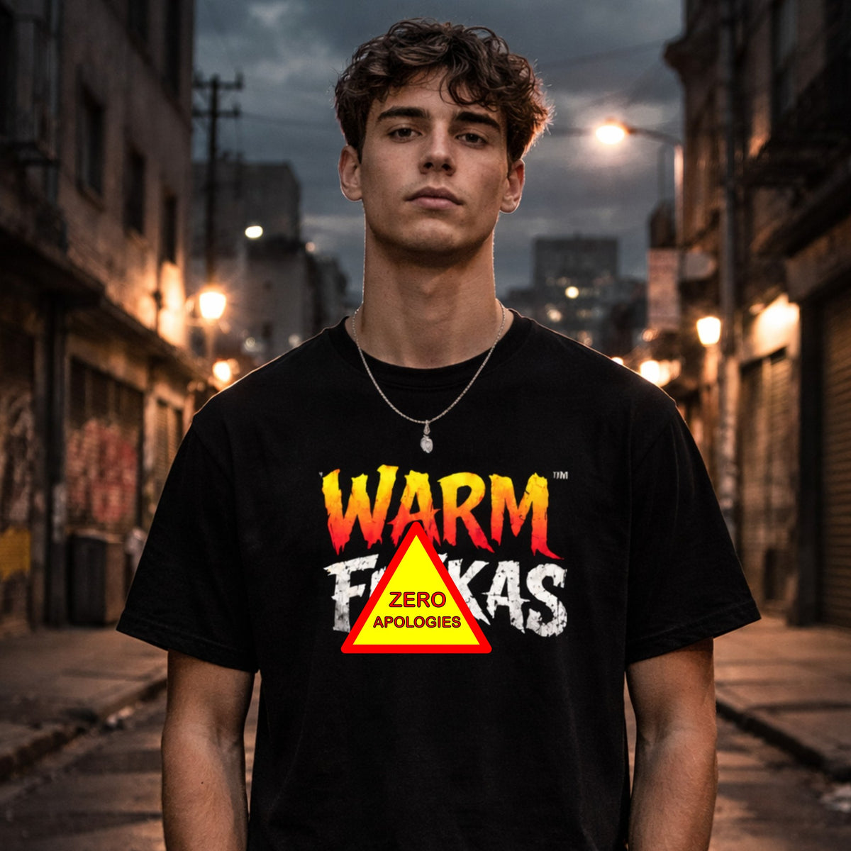 A young man wearing a black graphic t-shirt with a 'Zero Apologies' print, standing in a moody, dimly lit urban alleyway at night.